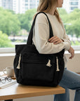 Black corduroy tote bag with tassel accents, zip-close pockets