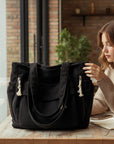 Black corduroy tote bag with front pocket and dangling tassels