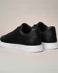 Black low-top trainers with heel tab and white rubber sole, rear view