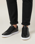 Black low-top trainers with lace-up closure and white sole worn with black trousers