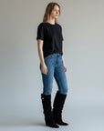 Black knee-high slouch boots with gold buckle, worn with blue jeans