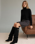 Black knee-high slouch boots on model, flat sole, gold buckle at cuff