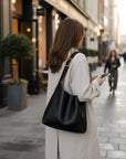 Black slouchy shoulder bag with gold-tone buckle strap, worn on shoulder