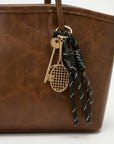 Close-up of textured brown tote bag with metal clip and braided tassel