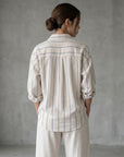 Back view striped button-up blouse in cream with blue vertical stripes and yoke pleats.