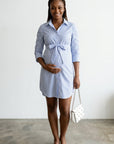Blue striped maternity shirt dress with button front and tie waist, holding white bag