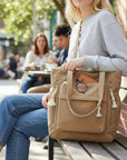 Beige corduroy tote bag with tassel charms and top handles, zip-close pockets