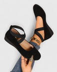 Black wedge ballet flats with ankle strap, crisscross upper, and gold bracelet detail.