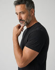 Men's black crew-neck T-shirt, short sleeves, side view with hand at collar.