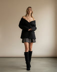 Black knee-high slouch boots on model, side profile, gold buckle at top
