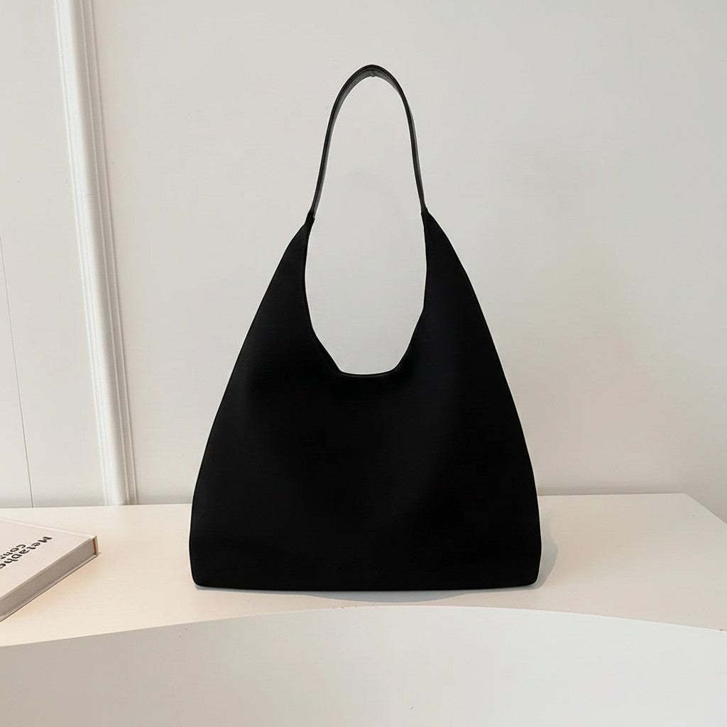 Black minimalist shoulder bag with open top and short handles on white surface.