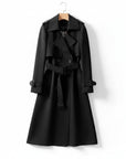 Black long trench coat with double-breasted front, belted waist, and shoulder straps.