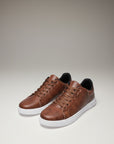 Brown low-top trainers with lace-up front and white rubber sole, angled view