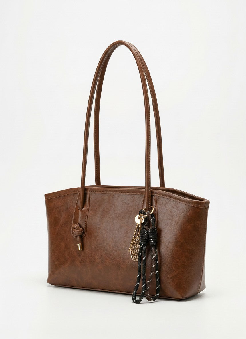 Textured brown tote bag with long handles and braided tassel charm
