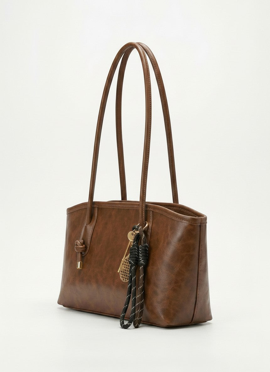 Textured brown leather tote bag with long handles and braided tassel key charm