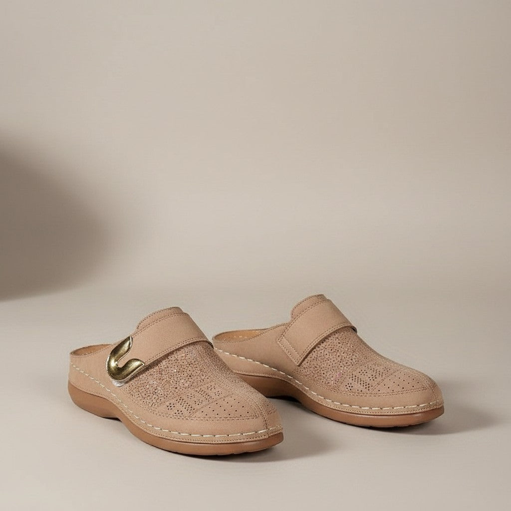 Beige slip-on orthopedic slippers with metal buckle accent and perforated upper.