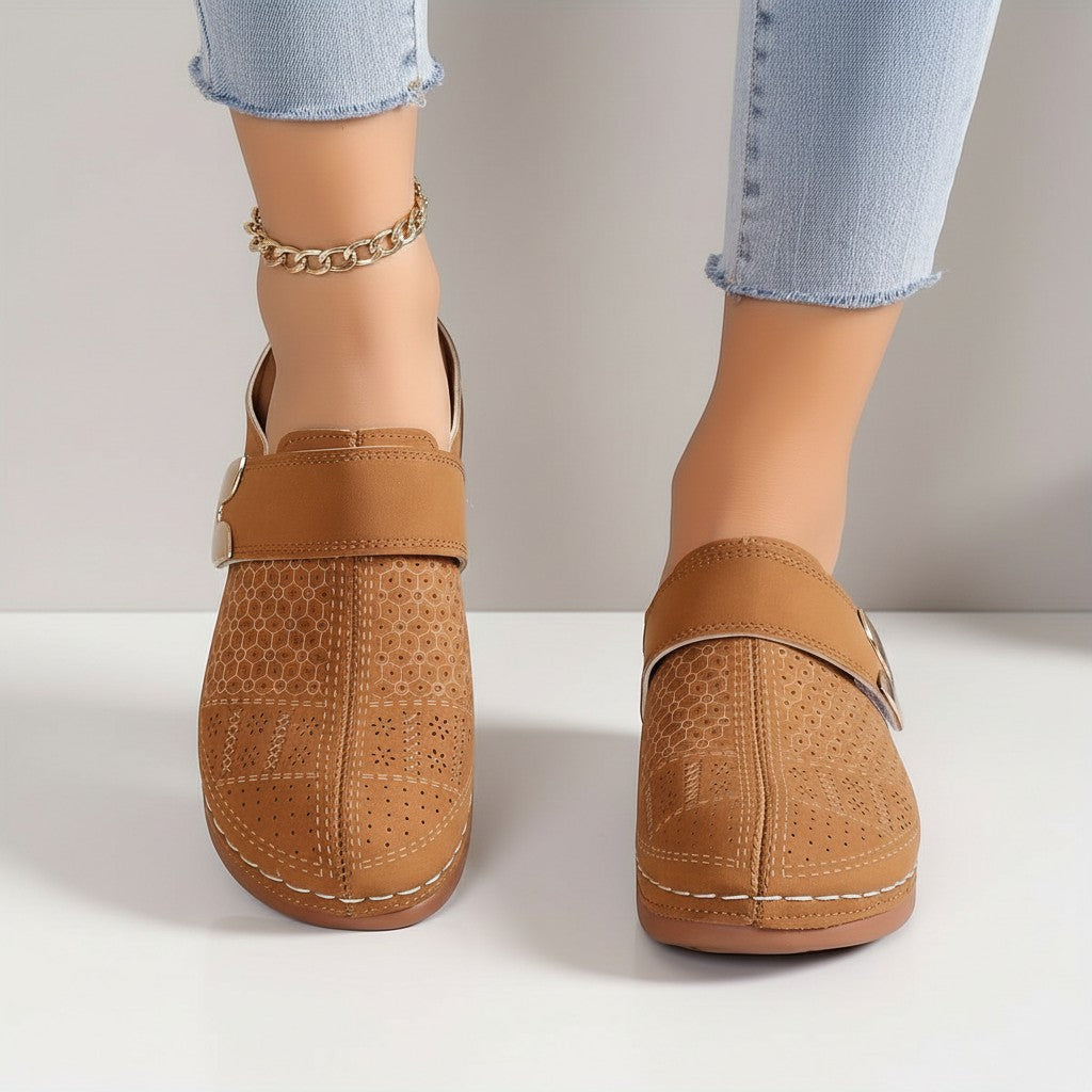 Tan mules on model feet with wide strap and metal buckle detail.