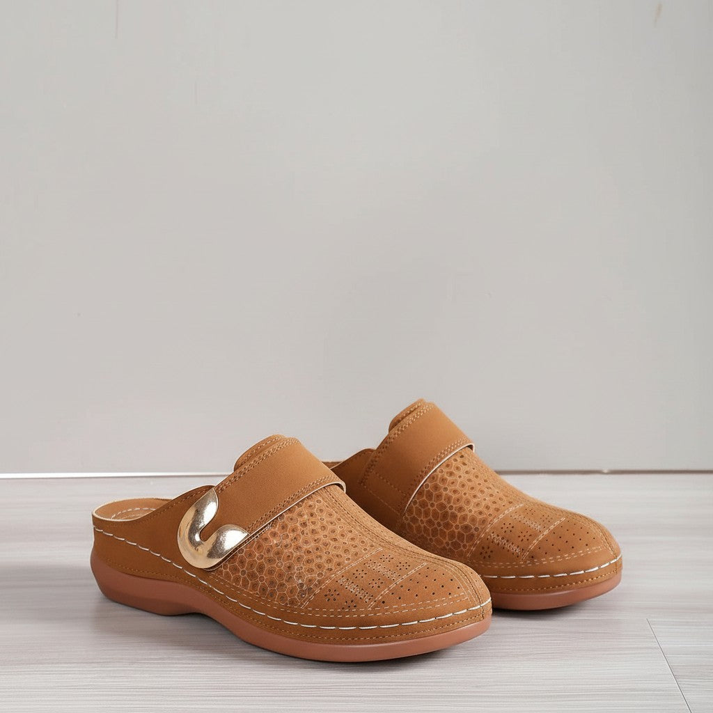 Tan slip-on slippers with curved metal buckle and perforated leather-style top.